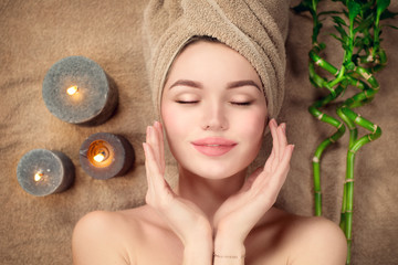 Beautiful spa woman with a towel on her head lying and touching face skin. Skincare. Beauty smiling model girl in spa salon