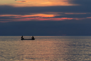 Fototapeta premium Two men fishing on the sea under sunset 