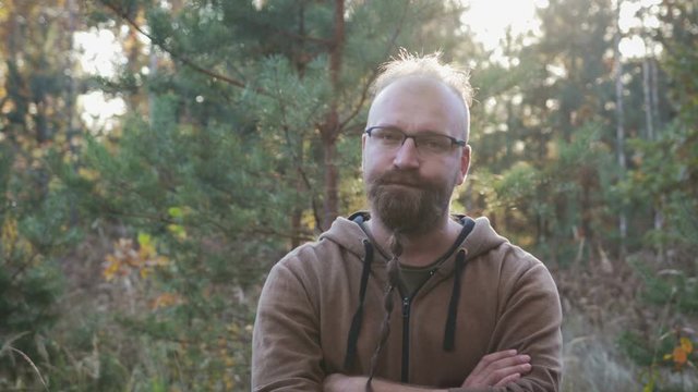 Crazy psychopath with a beard and glasses looking at the camera expressive and evil eyes and wants to kill you on the background of the forest. The concept of violence and cruelty