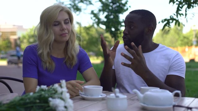 Bored female ignoring afro-american man and drinking coffee in cafe, bad date