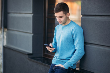 Fototapeta premium Young man is using the phone on the street. Handsome guy stand in front of window