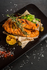 Grilled big fish steak on the black wooden background