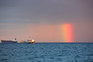 Seascape with amazing rainbaw half covered with heavy rainy clouds in sky, intensively colored, three ships on horiozn