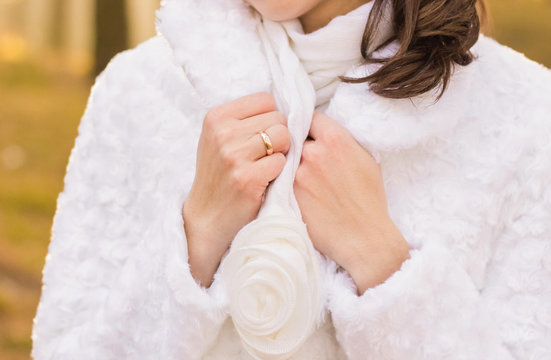 Closeup view of hands of elegant white bride with golden ring at finger. Bride wearing cute scarf and warm coat. Horizontal color photography.