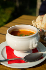 Fresh made vegetables cream soup served in white bowl with bread on outdoor terrace in sunlight