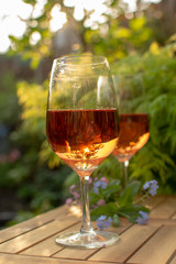 Two cold rose wine glasses served on outdoor terrace in garden with flowers in sunny day