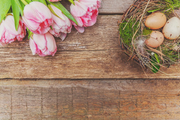 Spring greeting card. Easter eggs in nest with moss and pink fresh tulip flowers bouquet on rustic shabby wooden background. Easter concept. Flat lay top view copy space. Spring flowers tulips