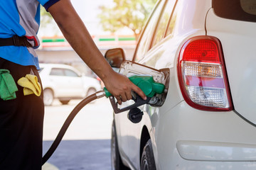 white car refueling gasoline by auto dispenser nozzle at petrol station with warm sunlight