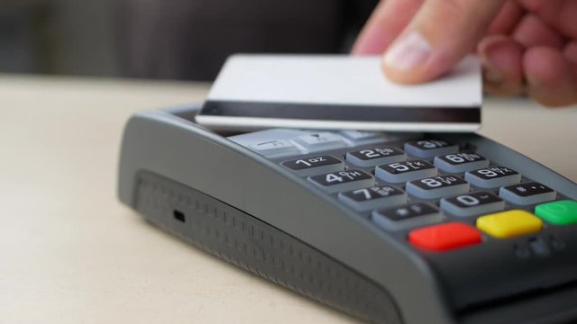 Hand of customer paying with contactless credit card with NFC technology. Credit card reader machine at bar counter with male holding credit card. Finger entering the PIN code