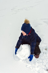 Fototapeta na wymiar little boy makes a snowman in winter. child rolls a snowball. happy kid plays and smiles. Emotion and happiness on children