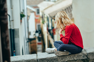 Young blonde tourist woman sitting outdoors looking a beautiful narrow street