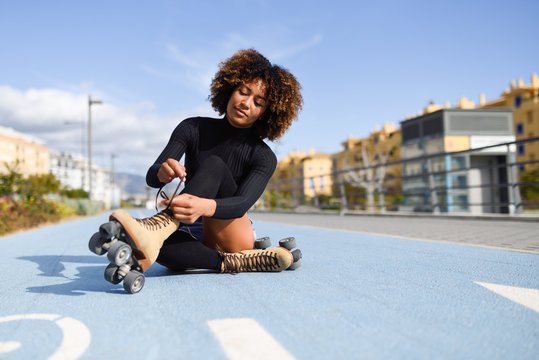 Young smiling black girl sitting on bike line and puts on skates.