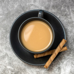 Top view of black cup of coffee with pastry on grey background