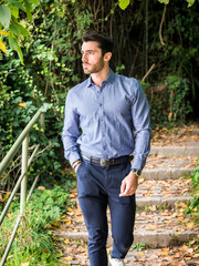 Attractive young man standing in nature setting by trees, looking away to a side