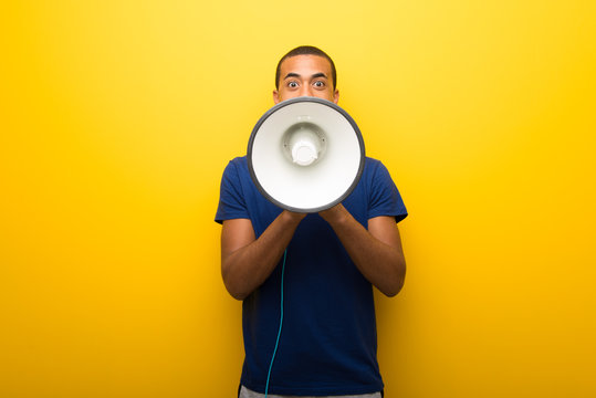 African American Man With Blue T-shirt On Yellow Background Shouting Through A Megaphone To Announce Something