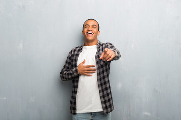 Young african american man with checkered shirt pointing with finger at someone and laughing a lot