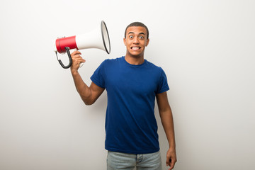 Young african american man on white wall taking a megaphone that makes a lot of noise