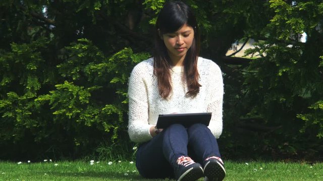Asian woman reading a ibook at the park in a lovely day, using Ipad, 4k
