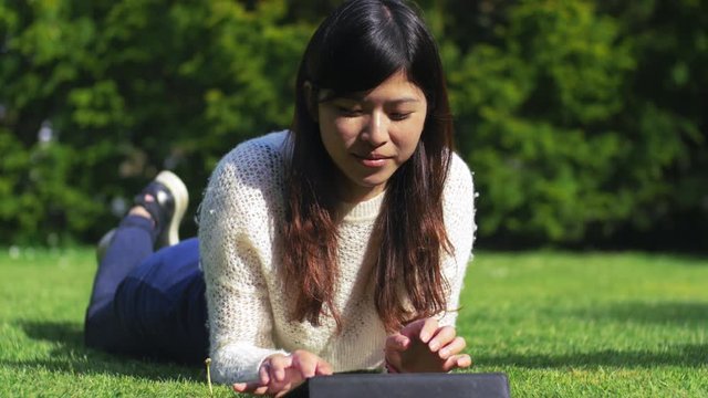 Asian woman eading a ibook at the park in a lovely day, using Ipad, 4k