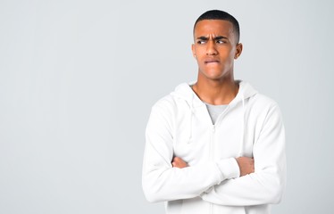 Dark-skinned young man with white sweatshirt having doubts and with confuse face expression while bites lip. Questioning an idea on grey background