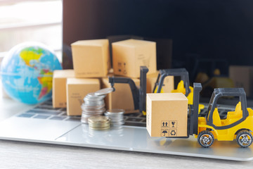 Mini forklift truck load cardboard box, stack of coins and pile of boxes on laptop keyboard with...