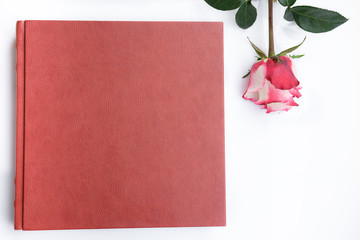 Red leather covered wedding album and rose lies on white background.