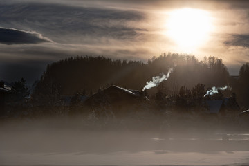 Smoke from the chimneys of a mountain village in the cold of the entrance at sunset