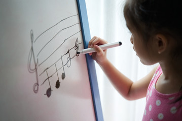 Young Asian girl kid winging music key on standing whiteboard. She practicing write down the key...