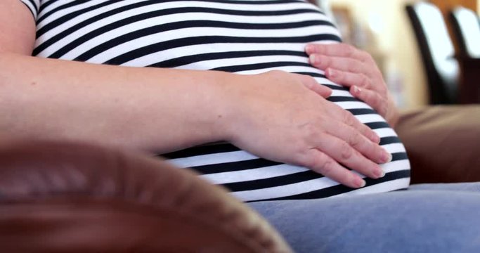 Close Up Of Pregnant Woman Sitting At Home Rubbing Stomach Lovingly