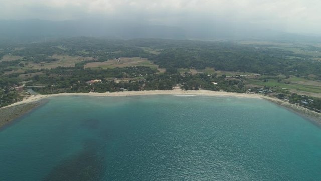tropical beach Cabugao with white sand and palm trees in the Philippines, Luzon. Aerial view coast with beach and turquoise water.