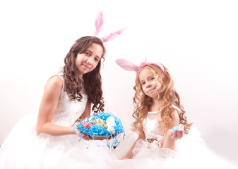 Obraz na płótnie Canvas two girls with easter eggs and bunny's ears on white background