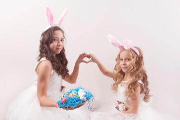 Obraz na płótnie Canvas two girls with easter eggs and bunny's ears on white background