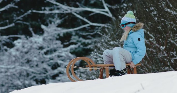 CU Cute little girl child preparing for a sledge ride down the hill. Child plays outdoors in snow, winter fun. 4K UHD 60 FPS SLOW MOTION