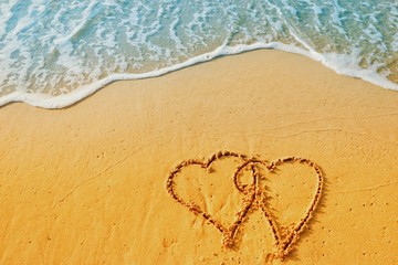 Valentine's day concept, two heart shape writing on sand beach with blue waves ocean.
