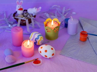 Easter decor, painted eggs, paints, brushes, lighted pink candles on a lilac background, preparation for the Easter holiday, seasonal spring celebrations