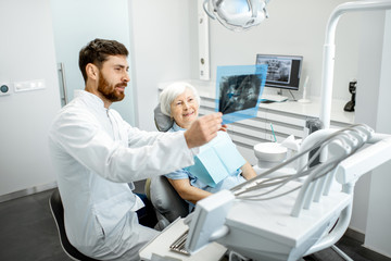 Happy elder woman during the consultation with handsome dentist showing panoramic x-ray in the dental office