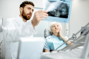 Worried elder woman during the consultation with handsome dentist showing panoramic x-ray in the...