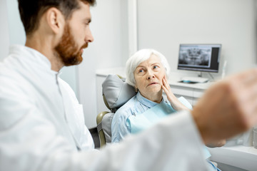 Worried elder woman during the consultation with handsome dentist showing panoramic x-ray in the dental office