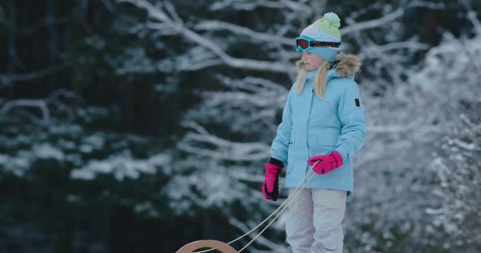 CU Cute little girl child preparing for a sledge ride down the hill. Child plays outdoors in snow, winter fun. 4K UHD 60 FPS SLOW MOTION