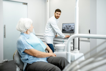 Dentist showing panoramic shot of the jaw on the computer to the elder woman during the consultation in the dental office