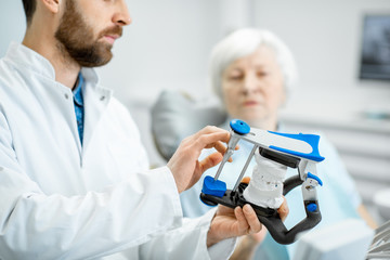 Dentist showing artificial jaw during the consultation with elder woman in the dental office