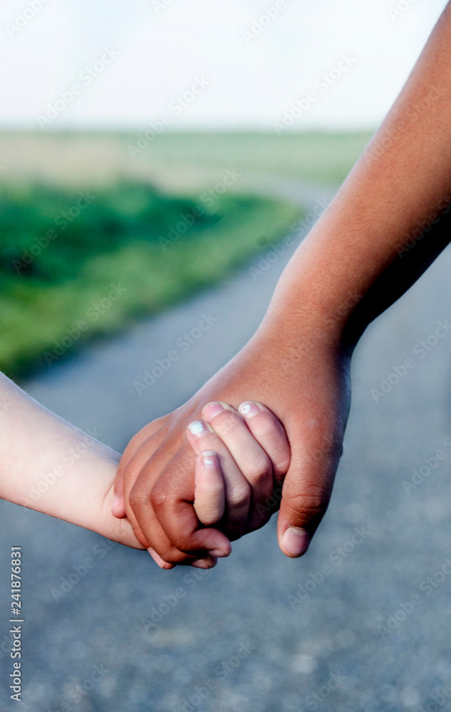 Wall mural Refugee girl holding hands with a white girl on the way on the countryside, closeup