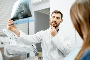 Fototapeta premium Handsome dentist checking panoramic x-ray of a jaw during the medical consultation with woman patient in the dental office