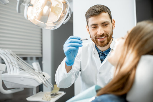 Handsome dentist making dental examination to a young woman patient in the dental office