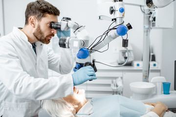 Male dentist examining senior woman looking on the teeth with professional microscope in the...