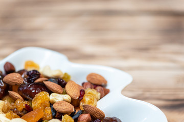 Dried fruits in white plate on wooden table, copy space for text. Mix of different varieties of nuts and berries, vitamins