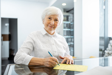 Beautiful senior woman signing some medical documents stannding at the hospital reception