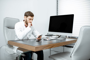 Handsome doctor sitting in the luxury medical office with computer
