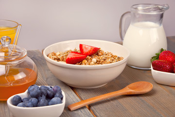 A plate with muesli, strawberries, juice, honey and milk on a wooden background.