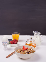 A plate with muesli, strawberries, juice, honey and milk on a white background.